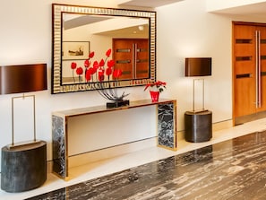 Un área de recepción moderna con una consola de mármol, un espejo grande y un arreglo floral rojo.