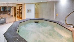 A modern indoor swimming pool with a glass enclosure, a wooden deck, and a view of a gym area. - Comfortable Apartment in London Near Trafalgar Square (London)
