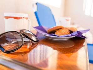 A wooden table with a pair of sunglasses, a white mug with a red stripe, and a plate of pastries.