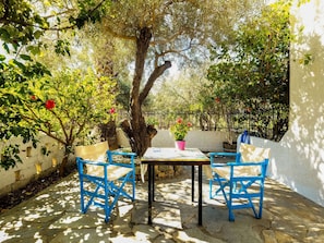 An outdoor patio with a table and blue chairs, surrounded by trees and a white wall. - Elegant Holiday Home in Palaiochora near Beach (Kantanos-Selino)