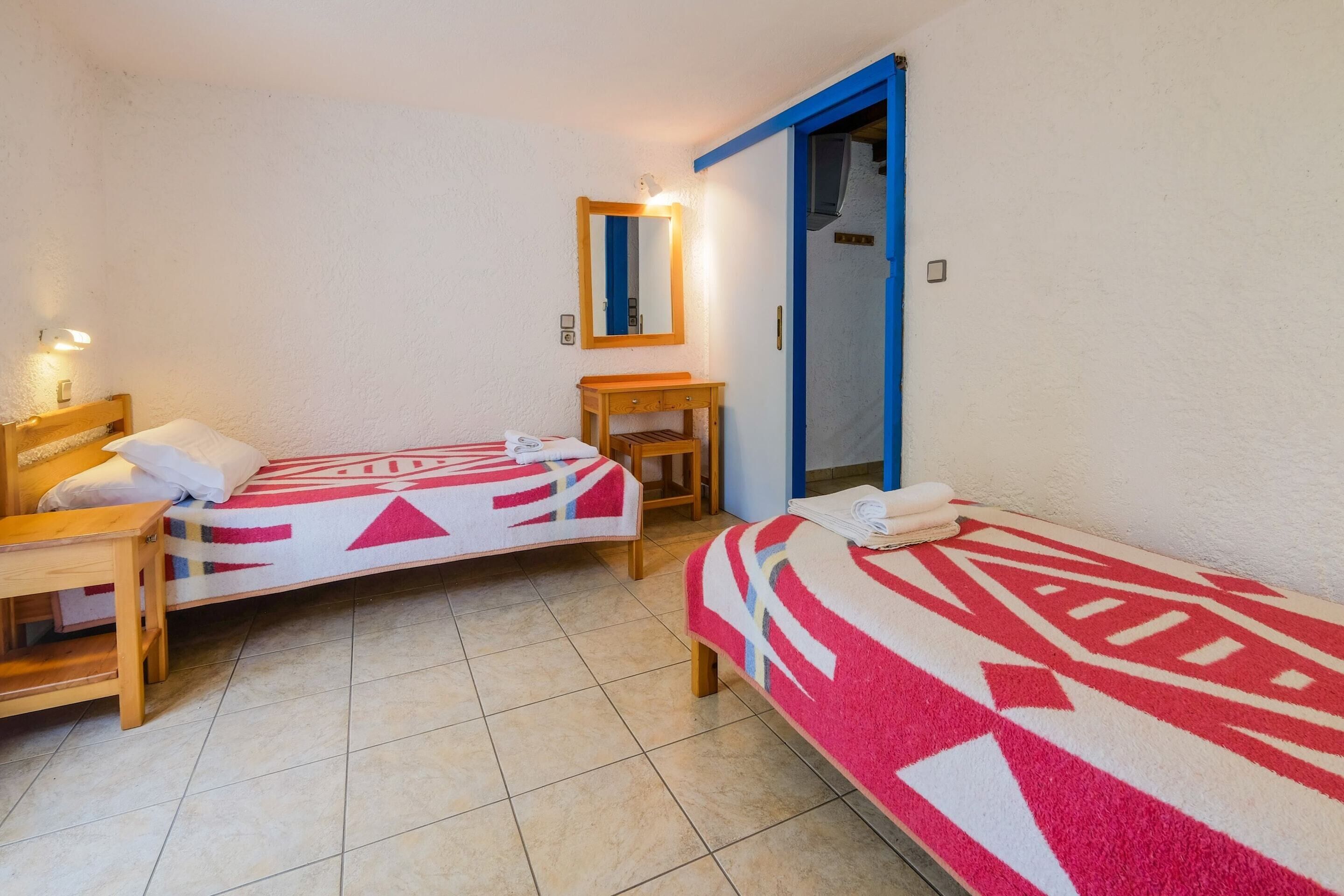 Een kleine, schone kamer met twee eenpersoonsbedden, een houten nachtkastje, een tafeltje en een spiegel.