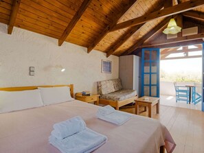 A cozy bedroom with a wooden ceiling, a bed with white linens, a small table, a chair, and a view of the outdoors through a blue door. - Tranquil Holiday Home in Palaiochora near Sea Beach (Kantanos-Selino)