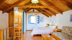 A cozy room with wooden beams, a bed, a sofa, a desk, and a window with blue shutters. - Tranquil Holiday Home in Palaiochora near Sea Beach (Kantanos-Selino)