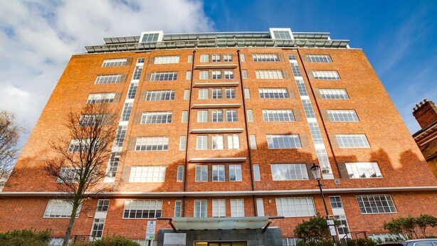 A multi-story brick building with a modern entrance and a car parked in front.