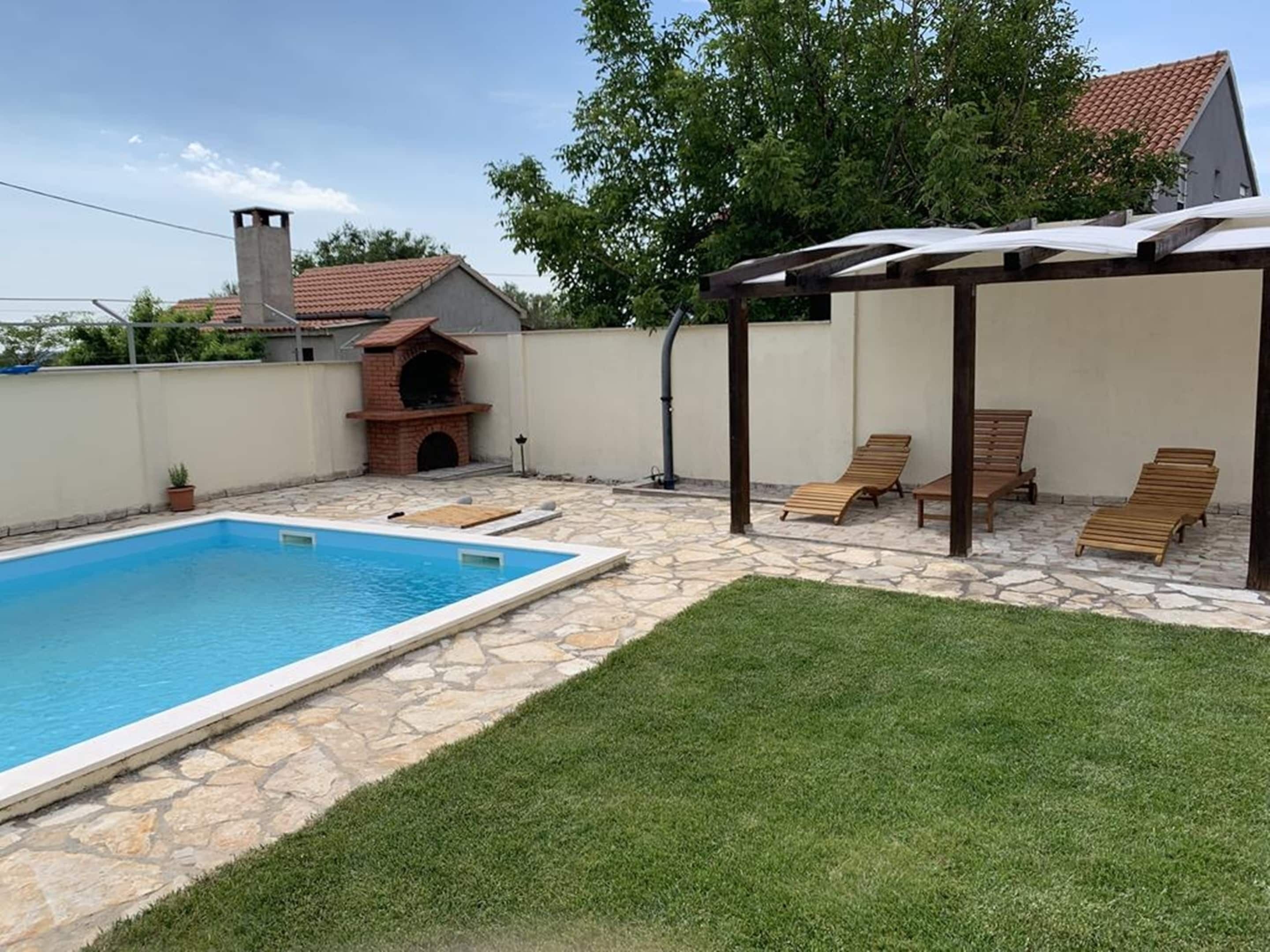 Un pati amb piscina, zona de barbacoa i espai d'estar cobert amb gandules.