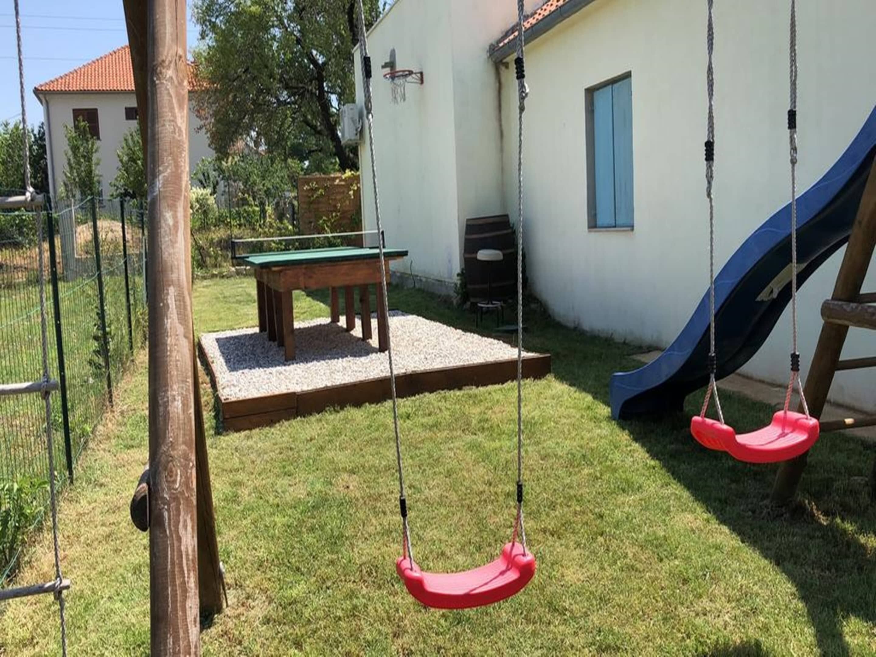 Un jardin avec une balançoire, un toboggan, une table et un bâtiment doté d’un toit rouge.