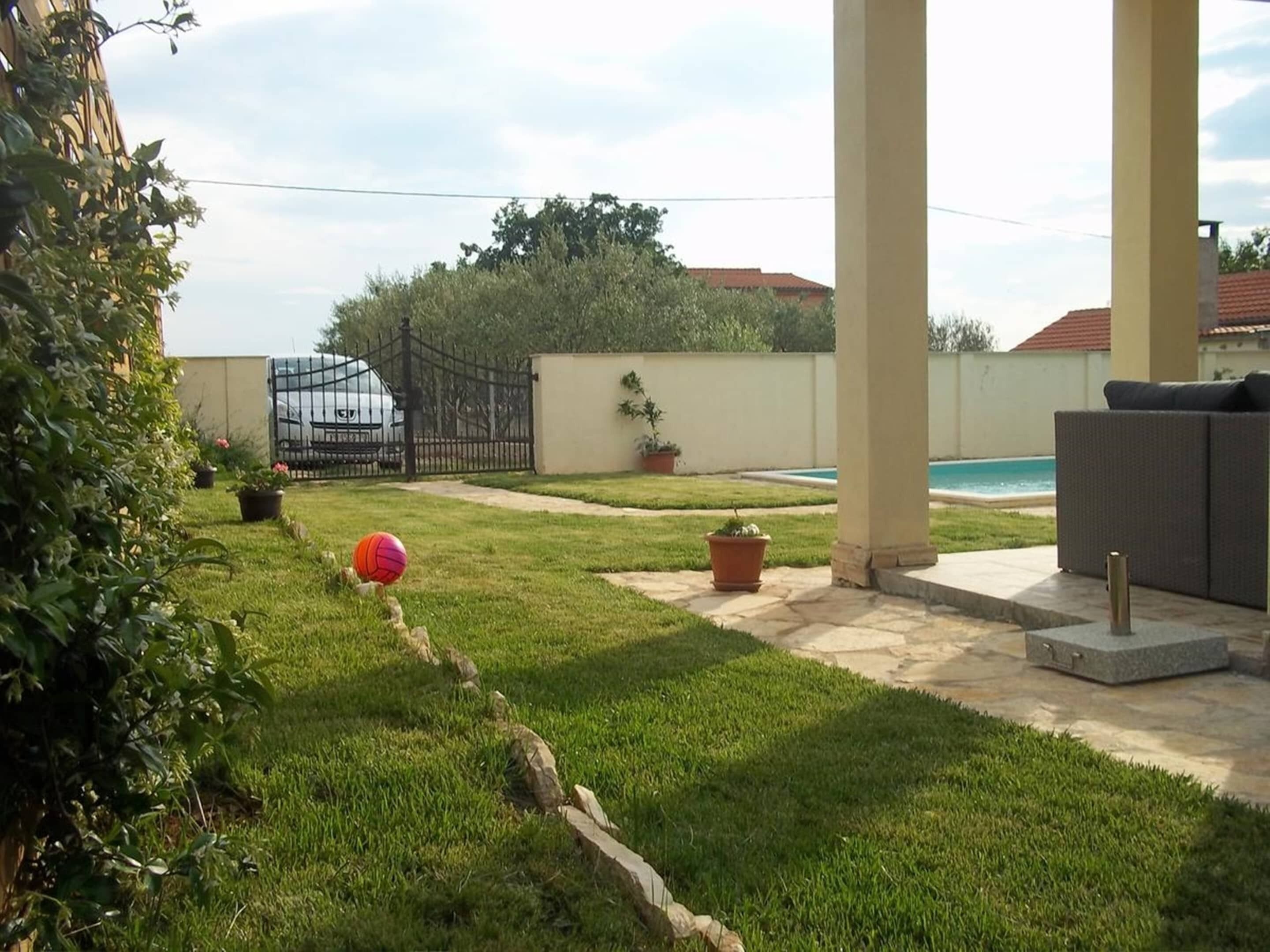 A backyard with a swimming pool, a covered patio area, and a garden with potted plants.