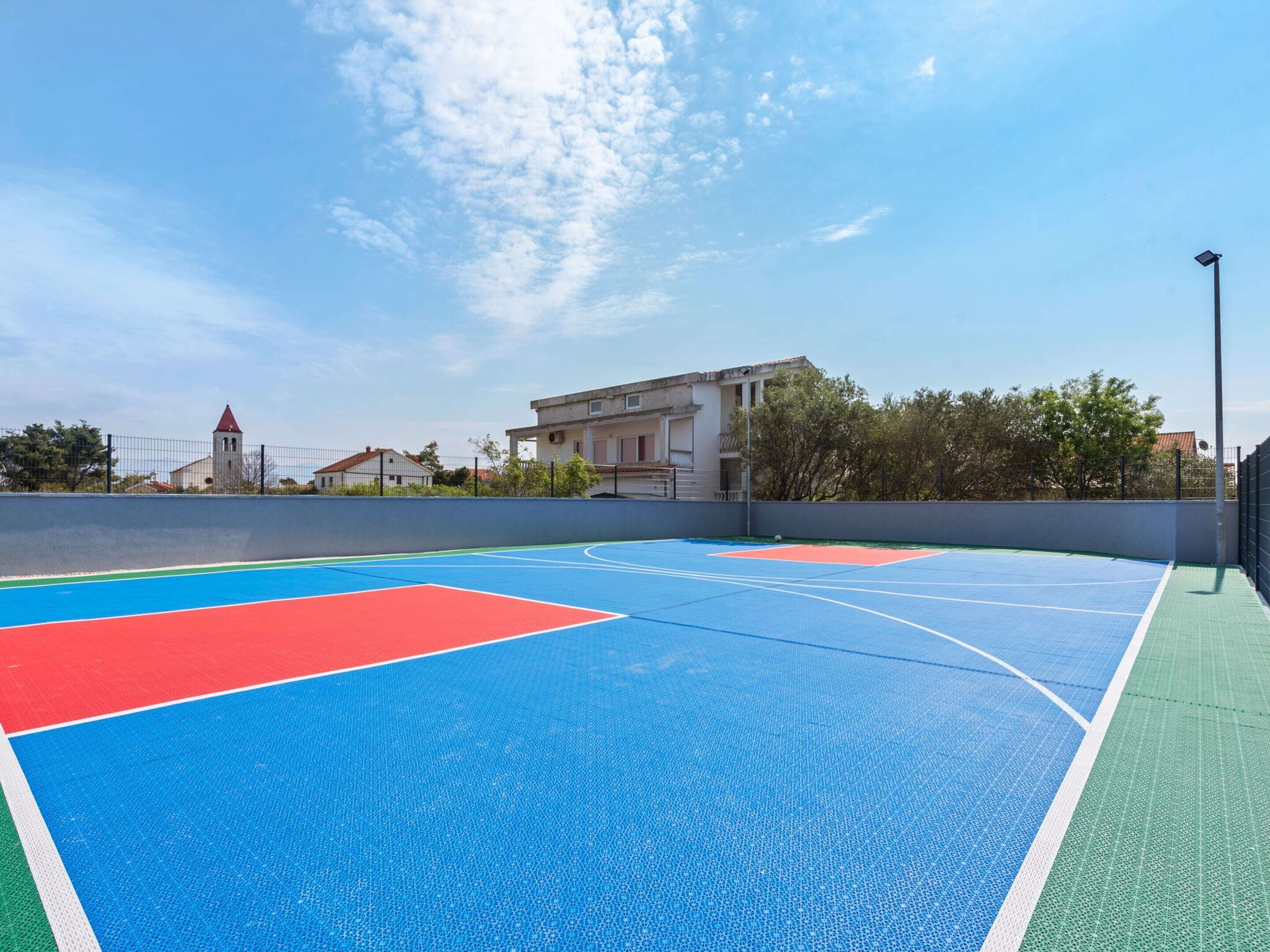 An outdoor basketball court with a clear blue sky, surrounded by buildings and trees.