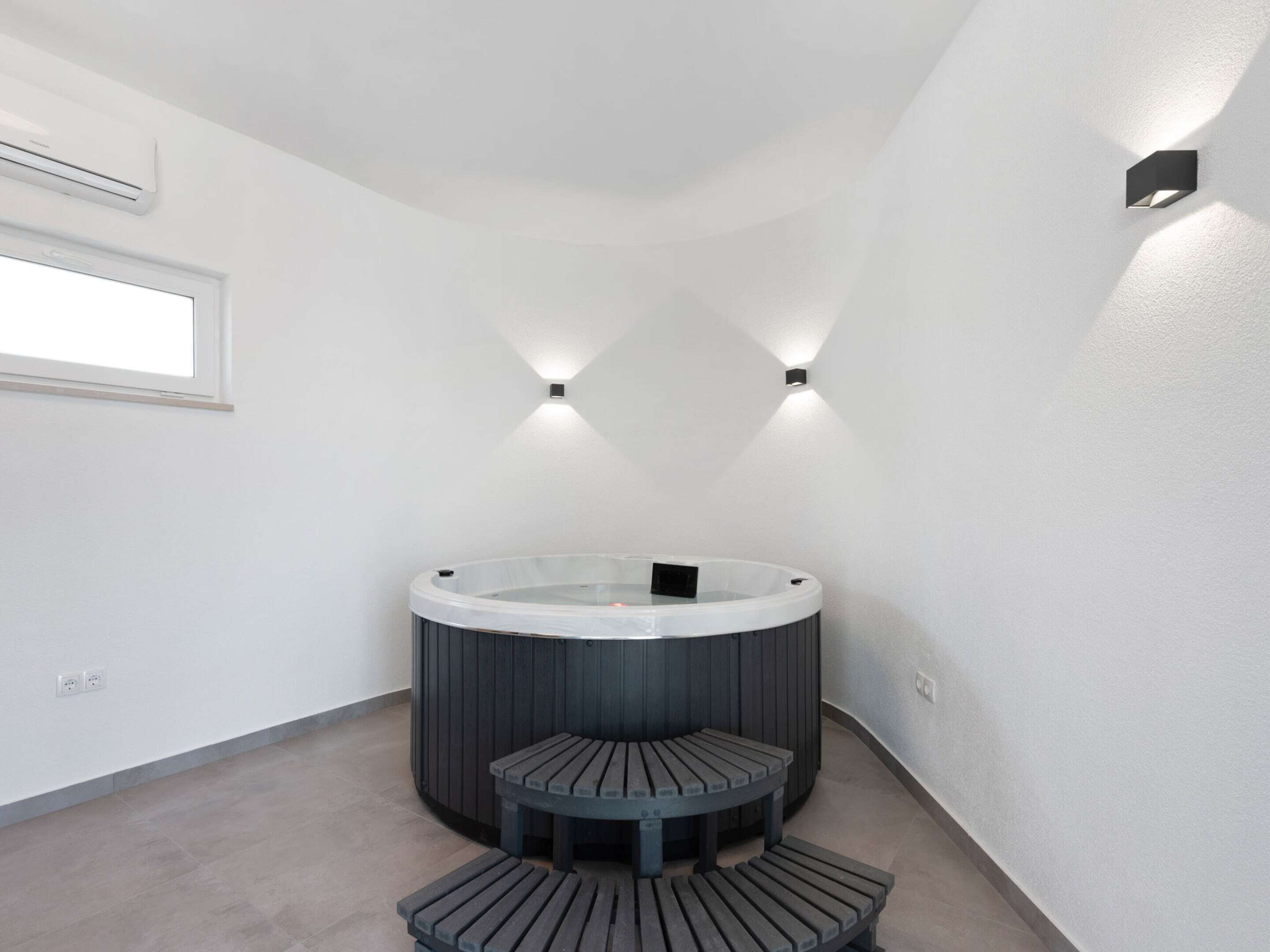 A modern bathroom with a freestanding bathtub, a small wooden bench, and two wall-mounted lights.