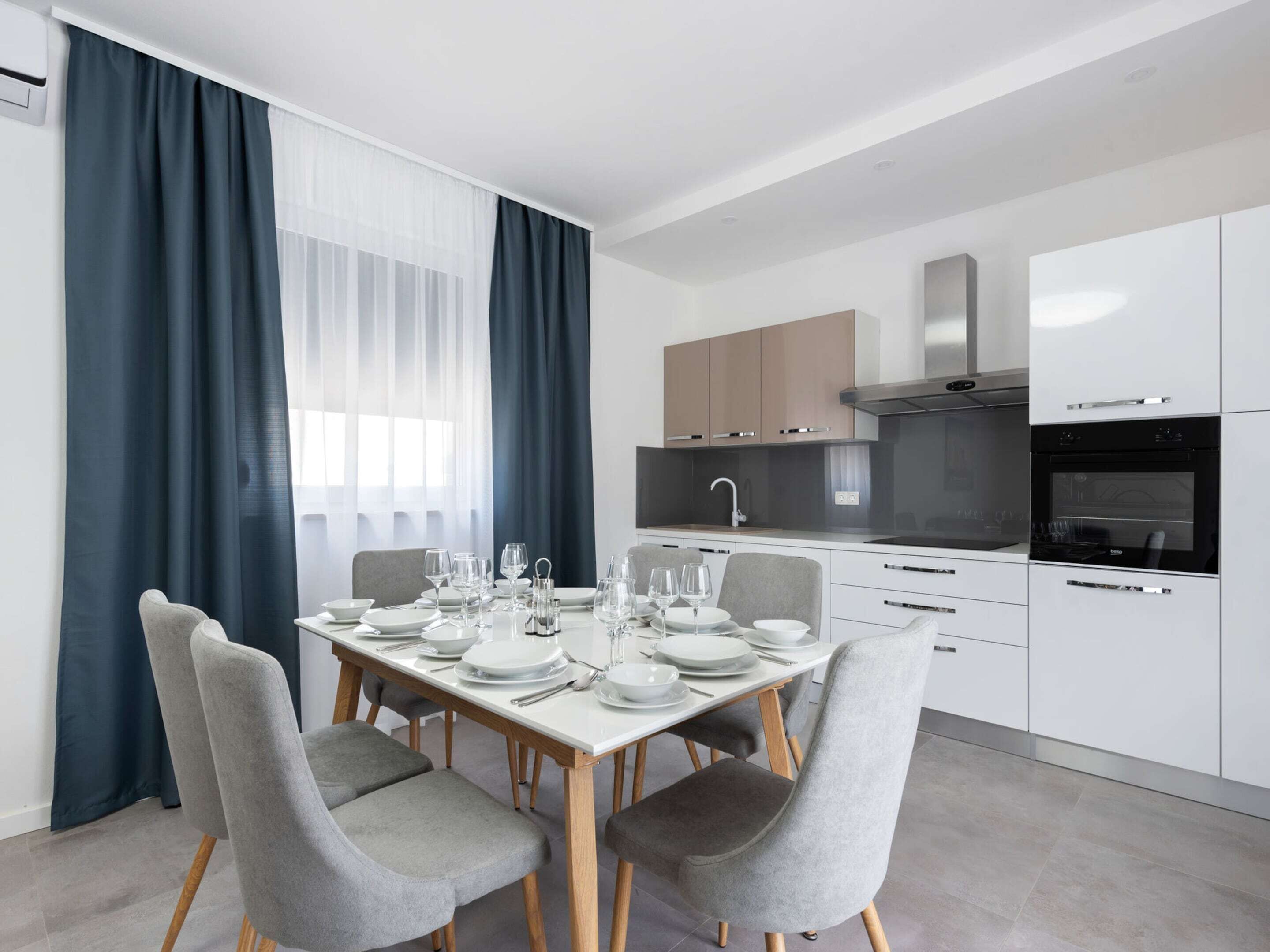 A modern kitchen with white cabinets, a built-in oven, and a stainless steel range hood.