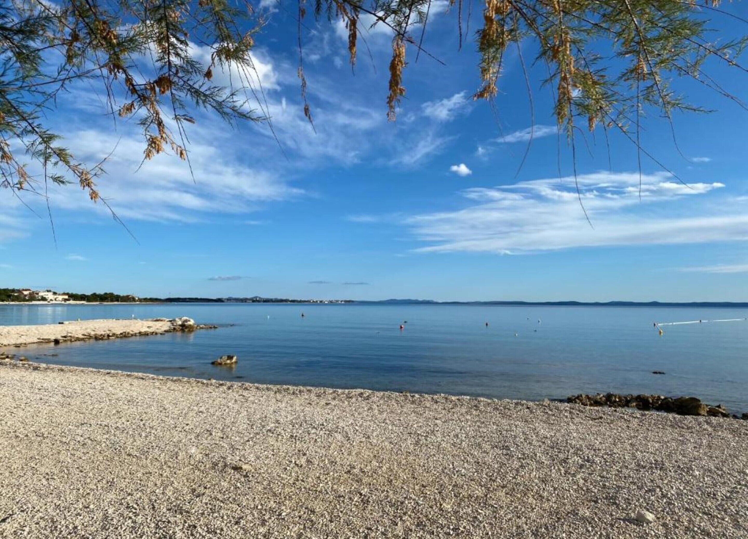 Uma praia de pedrinhas com águas calmas e terra ao longe.