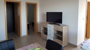 A room with a TV on a wooden cabinet, a desk, and a chair. There are two doors leading to other rooms. - Contemporary Apartment in Neviđane near Sea  (Pasman)