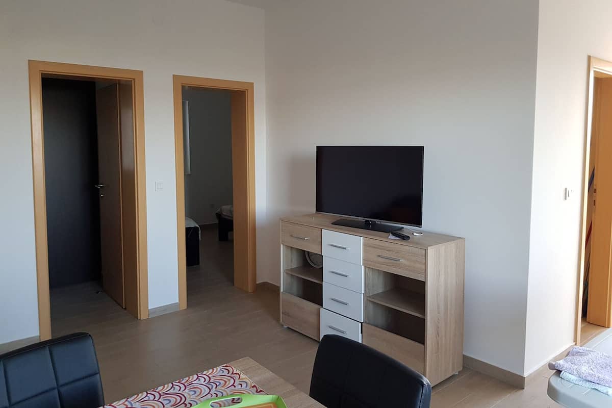 Une pièce avec un téléviseur posé sur un meuble en bois, un bureau et une chaise. Deux portes donnent sur d’autres pièces.