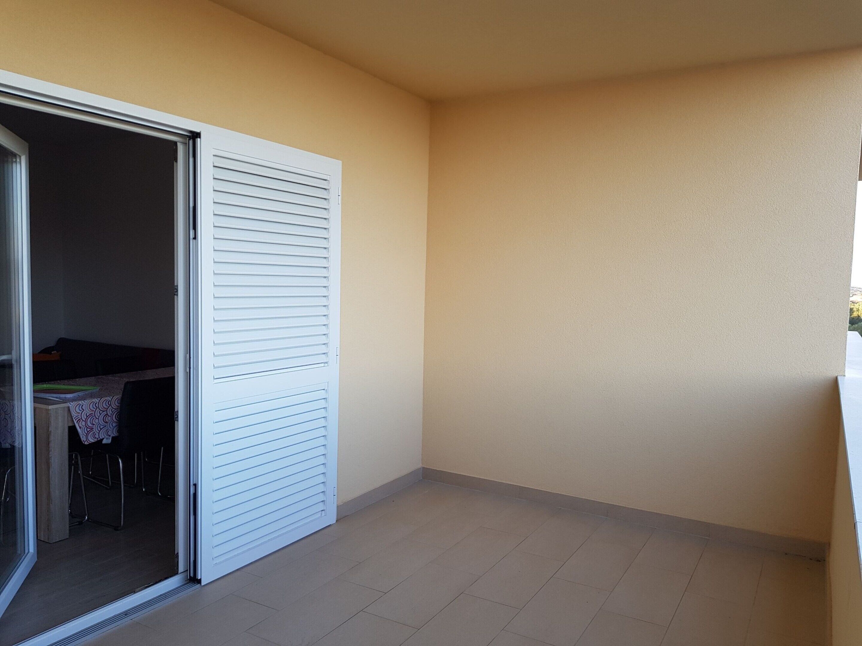 A small, enclosed balcony with a sliding glass door leading to a room.