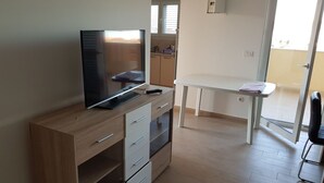 A modern living room with a flat-screen TV, wooden furniture, a dining table, and a sliding glass door leading to a balcony. - Contemporary Apartment in Neviđane near Sea  (Pasman)