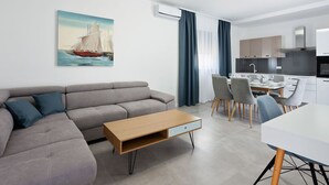 A modern living room with a grey sofa, a wooden coffee table, and a dining area with a white table and chairs. - Seaside Comfort on Vir Island (Vir)
