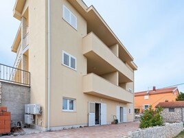 Un edificio residencial de varios pisos con balcones, unidades de aire acondicionado y un acceso pavimentado.