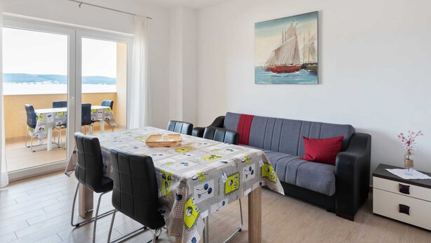 Un salon moderne avec un balcon, un coin repas comprenant une table et des chaises, et un tableau représentant un voilier accroché au mur.