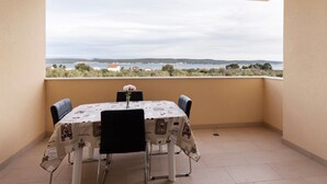 A balcony with a table and chairs, a view of the sea and hills, and a clear sky. - Simplistic Apartment in Neviđane with Balcony  (Pasman)