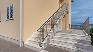 A set of outdoor stairs leading to a balcony with a metal railing, beige walls, and a clear sky in the background. - Simplistic Apartment in Neviđane with Balcony  (Pasman)