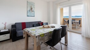 A modern living room with a dining area, a sofa, a table with a tablecloth, and a view of the sea through the balcony. - Simplistic Apartment in Neviđane with Balcony  (Pasman)