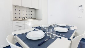 Et moderne spiseområde med hvide skabe, en flisebeklædt væg og et hvidt bord dækket med tallerkener, glas og bestik.