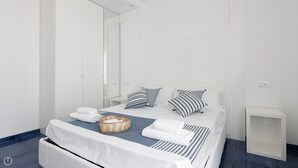 Et moderne hotelværelse med en stor seng, hvide vægge, et spejl og et lille natbord.