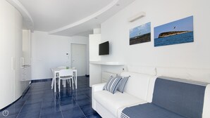 En moderne stue indrettet i hvide farver med en hvid sofa, et spisebord med stole og to billeder hængende på væggen.