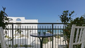 En balkon med havudsigt, en hvid bygning og et rundt bord med stole.