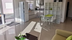 Une cuisine moderne avec des appareils électroménagers blancs, un coin repas doté d’une table en verre et un espace de vie avec un canapé.