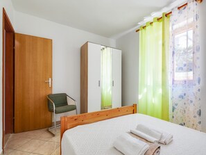A bedroom with a wooden bed, a green chair, a wardrobe, and a window with floral curtains.