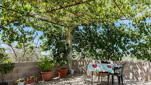 An outdoor patio area with a table and chairs under a pergola, surrounded by potted plants and a stone wall.