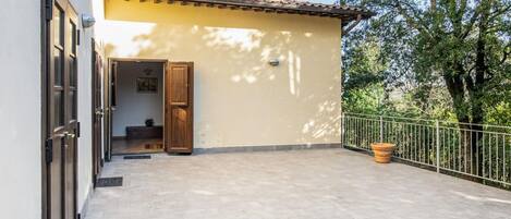 A covered patio area with a tiled floor, a wooden door, and a potted plant.