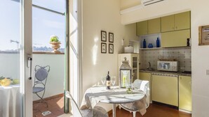 Ein Essbereich mit Tisch und Stühlen, Blick auf die Stadt durch ein großes Fenster und eine Küche mit gelben Schränken.