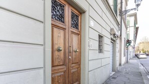 Eine doppelte Holztür mit einem Metallgitter, ein kleines Fenster darüber und ein gepflasterter Gehweg.