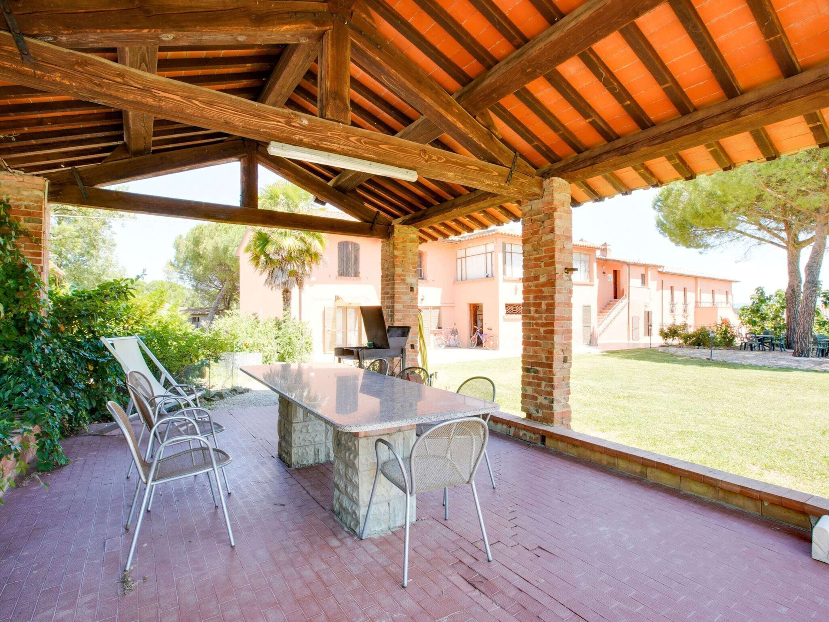 An outdoor patio with a stone table and metal chairs, a brick column, and a view of a residential area with buildings and trees.