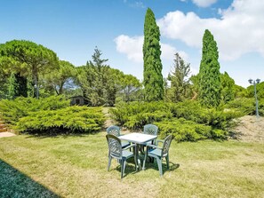 A garden with a table and chairs, surrounded by various trees and shrubs.