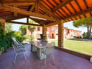 Une terrasse extérieure avec une table en pierre et des chaises en métal, entourée d’un mur de briques et offrant une vue sur un immeuble à la façade rouge.