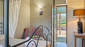 Une chambre à coucher avec un lit à baldaquin, une table de chevet avec une lampe, une fenêtre donnant sur l’extérieur et une porte menant à un patio.