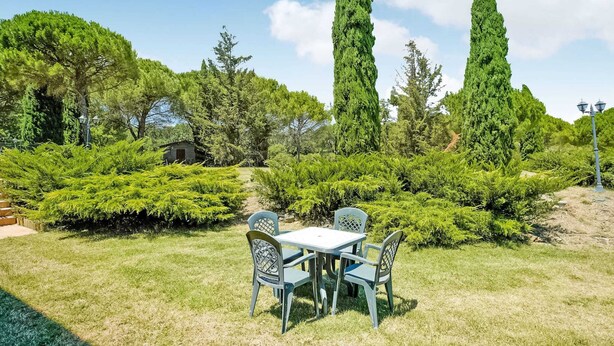 A garden with a table and chairs, surrounded by various trees and shrubs. - Holiday Home in Castiglione Near the Lake (Castiglione del Lago)