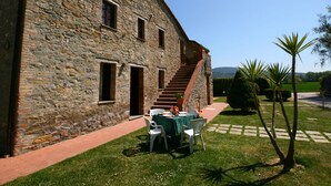 A stone building with a staircase leading to a covered area. There is a table with chairs outside, and a palm tree in the foreground. - Holiday Home in Magione Near Lake Trasimeno (Magione)