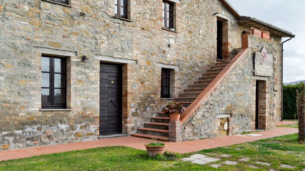 A stone building with a staircase leading to the upper floor, a black door, and a sign on the right side. - Holiday Home in Magione Near Lake Trasimeno (Magione)