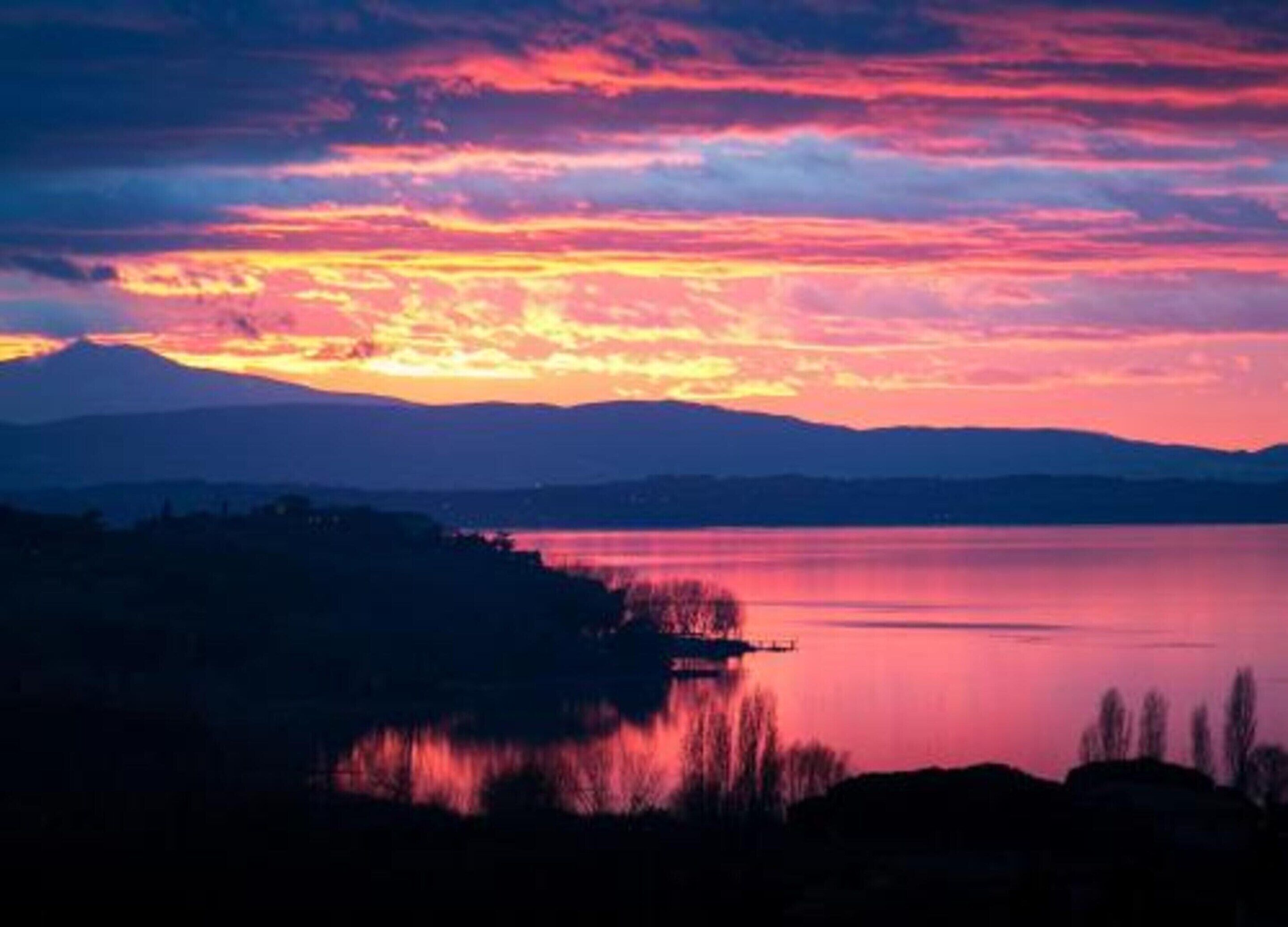 A sunset over a calm lake with distant mountains.