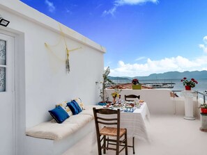 Ein Balkon mit Esstisch, einer Couch mit Kissen und Blick auf Meer und Berge.