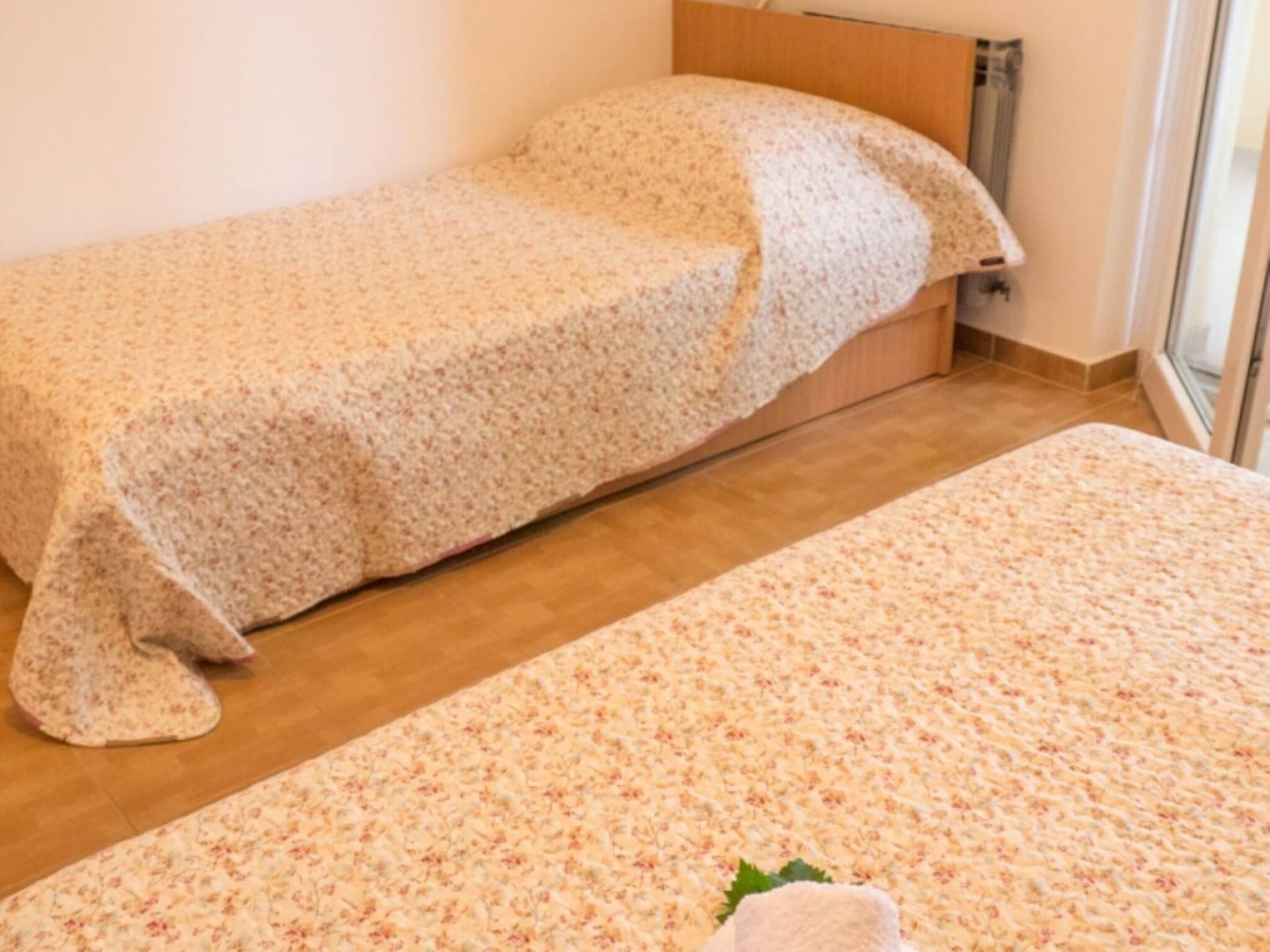 Habitación con dos camas cubiertas con ropa de cama de estampado floral, cabecera de madera y ventana que deja entrar luz natural.