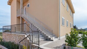 A two-story building with a stone base and a beige exterior. - Simplistic Apartment in Neviđane near Sea (Pasman)