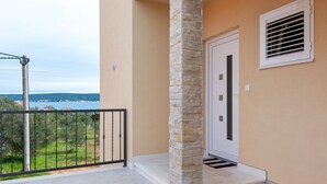A balcony with a stone pillar, a door with a vent, and a view of the sea and hills. - Simplistic Apartment in Neviđane near Sea (Pasman)