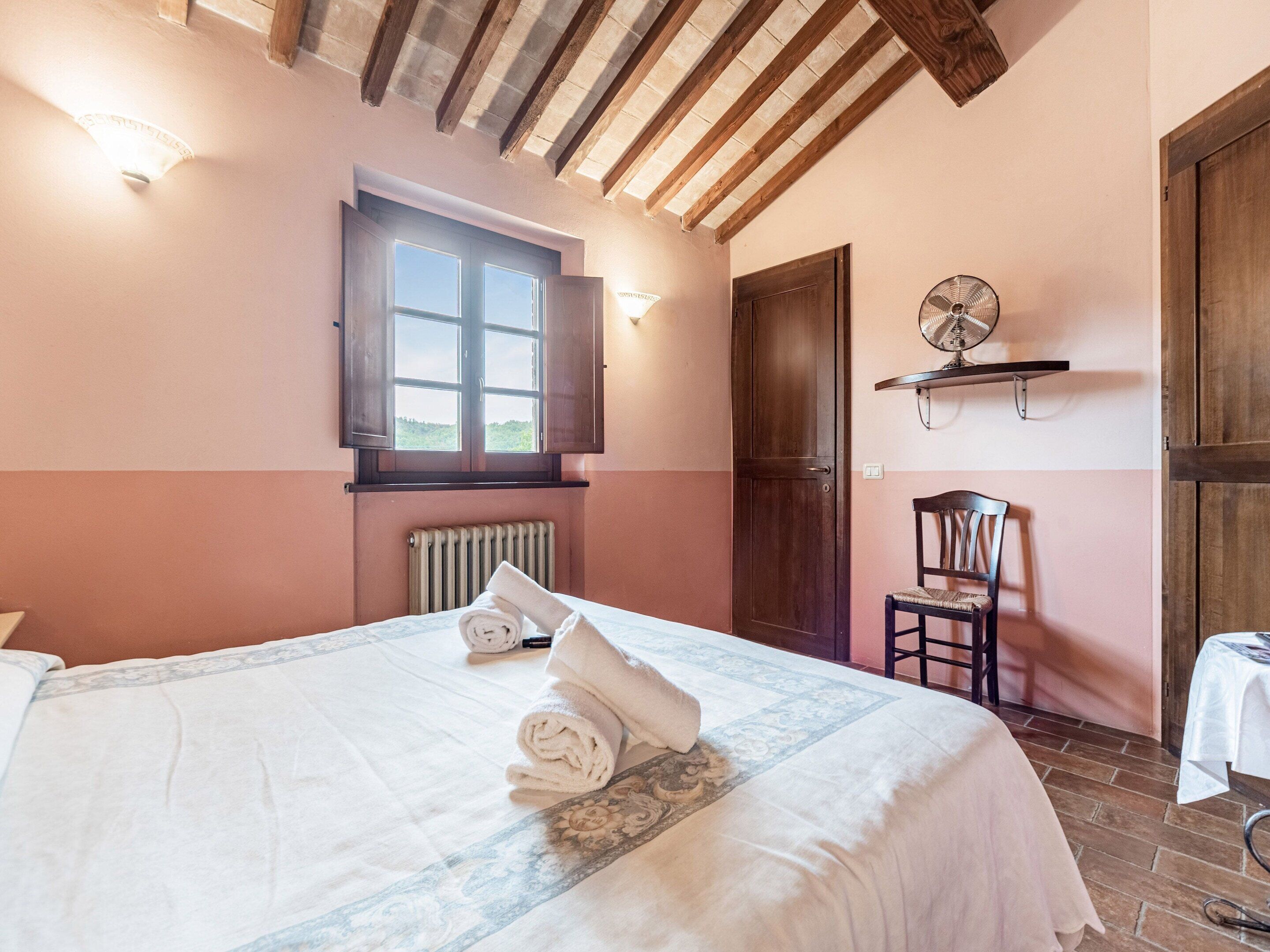 A bedroom with a bed, a window, a radiator, a wooden door, a chair, and a fan on a shelf.