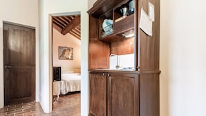 A kitchen with wooden cabinets, a sink, and a countertop. There is a bed with a white blanket and a painting on the wall. - Cottage in Umbria With Pool & Garden (Citta della Pieve)