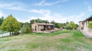 A stone house with a patio, surrounded by a grassy yard and trees. - Cottage in Umbria With Pool & Garden (Citta della Pieve)